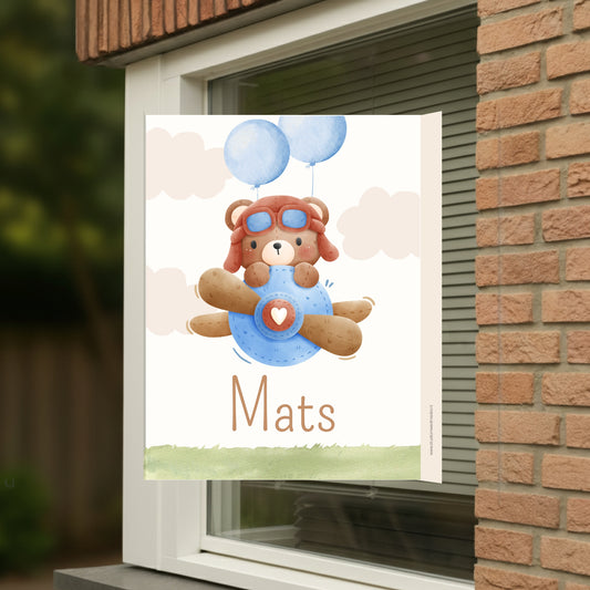 Geboortebord voor op het raam met naam en de afbeelding van een schattig beertje in een vliegtuig.
